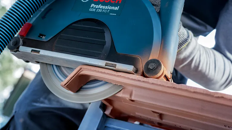 Une personne portant un équipement de sécurité coupe une tuile de toit avec une scie circulaire.