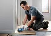 Une personne portant un équipement de sécurité coupe un plancher en bois avec un outil multifonction sans fil.