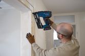 Une personne portant un équipement de sécurité installe des garnitures en bois à l’aide d’une cloueuse sans fil.
