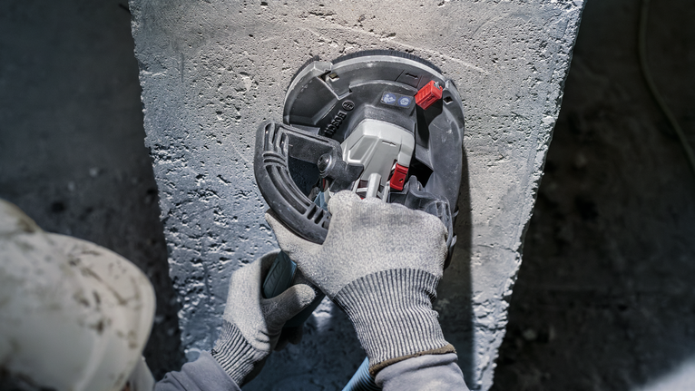 Une personne portant un équipement de sécurité broie du béton avec un outil électrique.