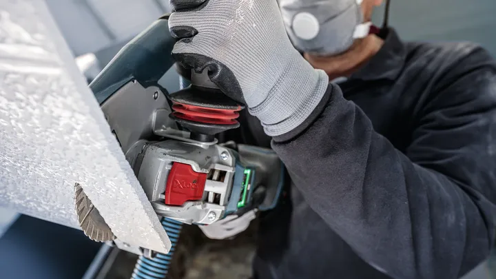 Une personne portant un équipement de sécurité coupe un panneau avec un outil électrique.