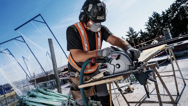 Une personne portant un équipement de sécurité coupe du bois avec une scie circulaire sur un chantier de construction.