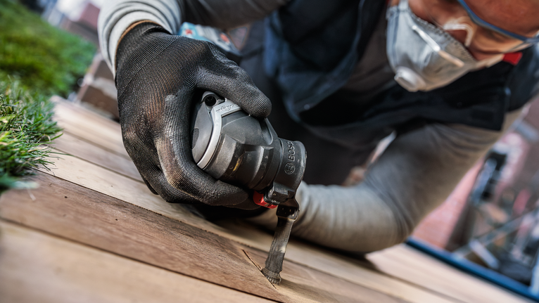 Une personne portant un équipement de sécurité utilise un outil électrique pour couper une planche de bois.