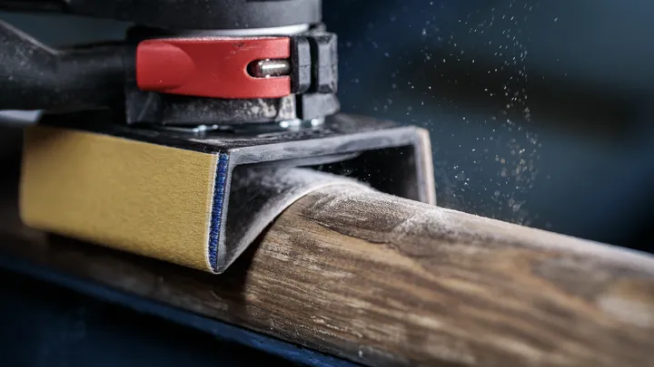 Ponceuse orbitale lissant une poutre en bois arrondie, particules de poussière de bois visibles.