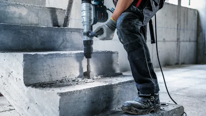 Une personne portant un équipement de sécurité utilise un marteau perforateur pour briser des escaliers en béton.
