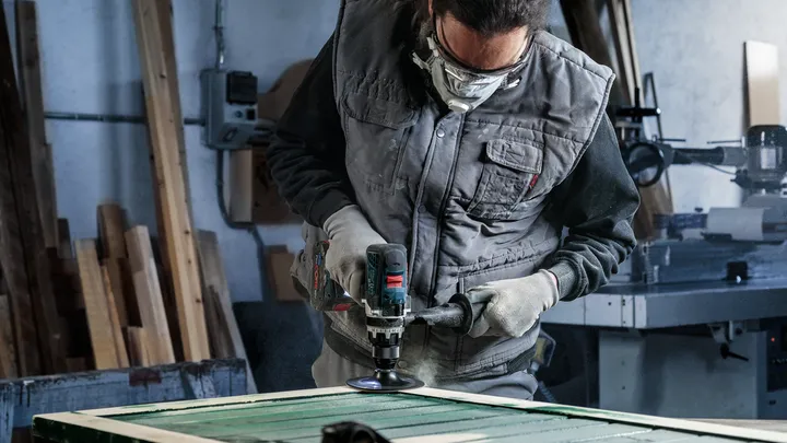 Une personne portant un équipement de sécurité polit une surface en bois avec un outil électrique.