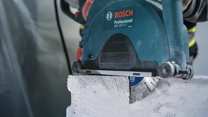 Une personne portant un équipement de sécurité utilise une scie circulaire pour couper un bloc de béton.