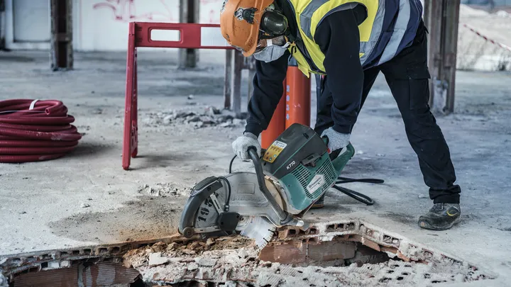 Une personne portant un équipement de sécurité coupe un sol en béton avec une découpeuse électrique.