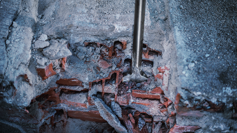 Marteau perforateur perçant un mur de béton et de briques endommagé.