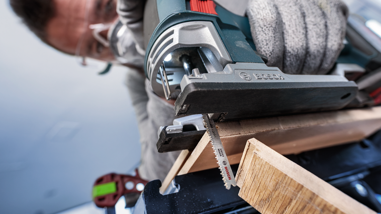 Une personne portant un équipement de sécurité utilise une scie sauteuse électrique pour couper un morceau de bois.