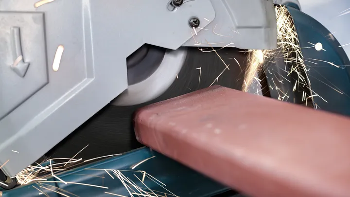 Une scie à métaux coupe une poutre en acier, produisant des étincelles brillantes.