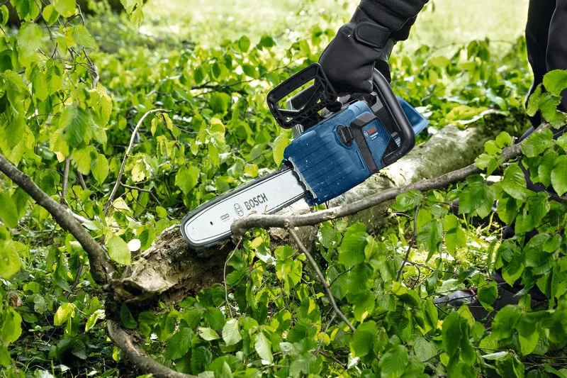 Une personne portant un équipement de sécurité coupe une branche d’arbre tombée avec une tronçonneuse sans fil.