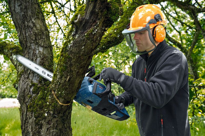 Une personne portant un équipement de sécurité coupe une branche d’arbre avec une tronçonneuse sans fil.