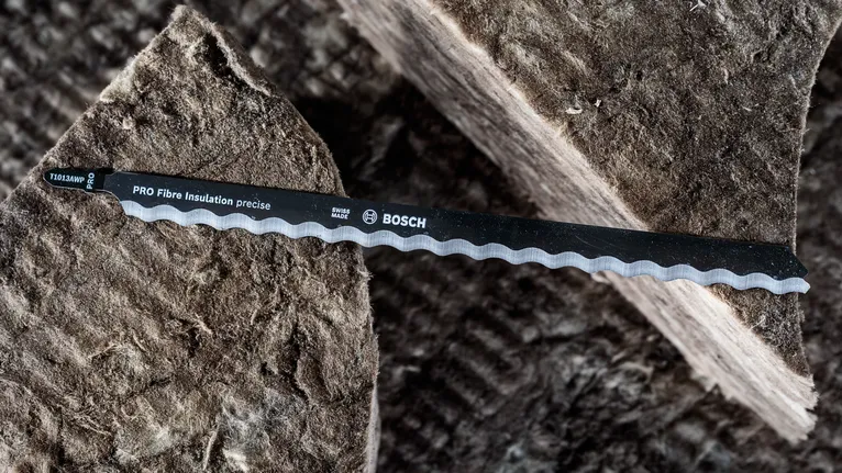 Lame de scie sauteuse dentelée posée sur d'épaisses feuilles de matériau isolant en fibres.
