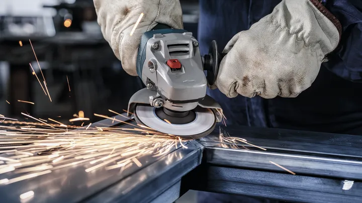 Une personne portant un équipement de sécurité utilise une meuleuse d'angle pour couper le métal, produisant des étincelles.