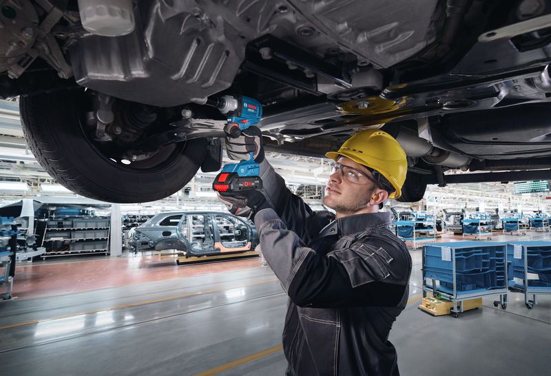 Une personne portant un équipement de sécurité utilise une clé électrique pour fixer des boulons sous le châssis d’un véhicule.