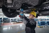 Une personne portant un équipement de sécurité utilise une clé électrique pour fixer des boulons sous le châssis d’un véhicule.