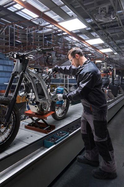 Une personne portant un équipement de sécurité utilise une visseuse à chocs pour assembler un cadre de moto.