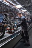 Une personne portant un équipement de sécurité utilise une visseuse à chocs pour assembler un cadre de moto.