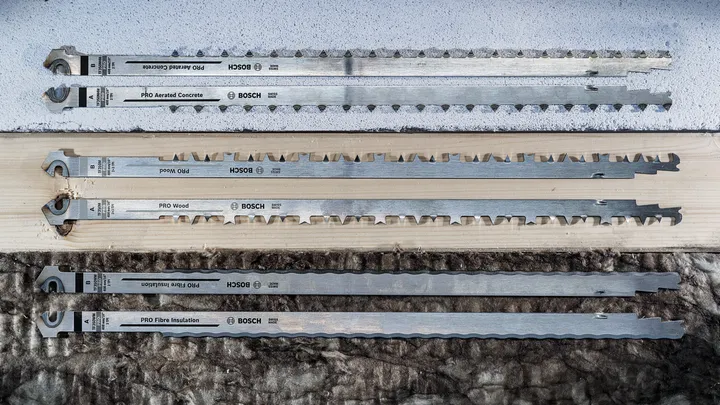 Quatre longues lames de scie alternative exposées sur du béton, du bois et des matériaux isolants.