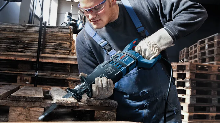 Une personne portant un équipement de sécurité utilise une scie alternative pour couper une palette en bois.