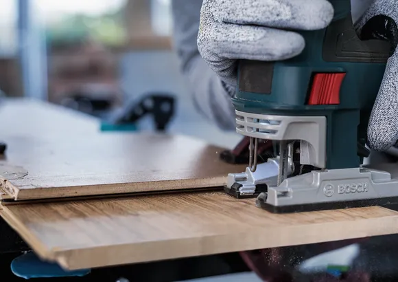 Une personne portant un équipement de sécurité utilise une scie sauteuse pour couper une planche de bois.