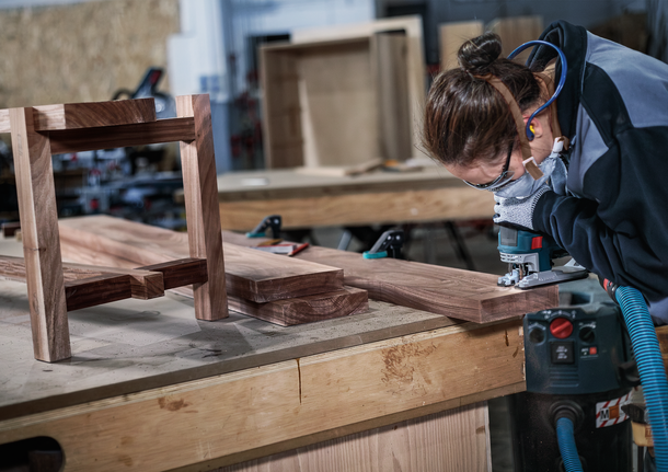 Une personne portant un équipement de sécurité façonne une planche de bois avec un outil électrique.