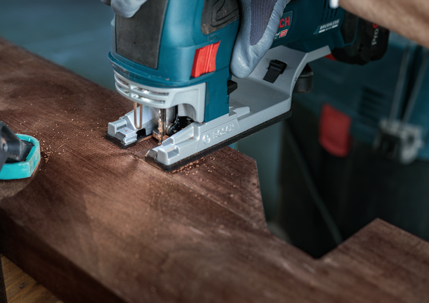 Une personne portant un équipement de sécurité utilise une scie sauteuse pour découper une forme dans une planche de bois.