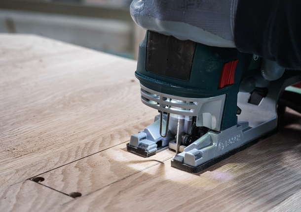 Une personne portant un équipement de sécurité utilise une scie sauteuse pour couper une section rectangulaire dans du bois.