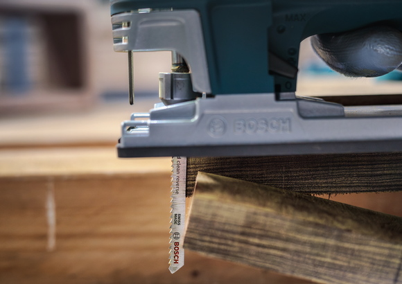 Une personne portant un équipement de sécurité utilise une scie sauteuse pour couper une planche de bois.