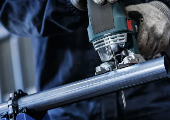 Une personne portant un équipement de sécurité utilise une scie sauteuse pour couper un tuyau métallique.