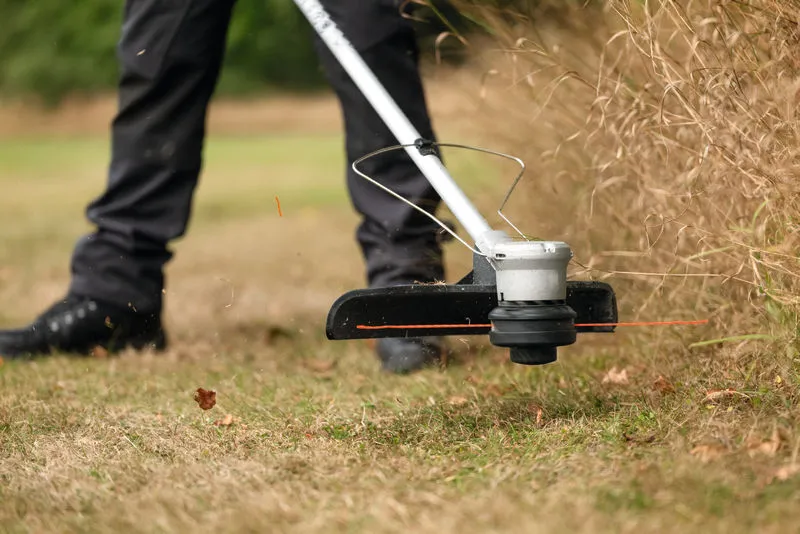 Une personne coupe l’herbe haute le long d’une bordure de pelouse avec un coupe-herbe sans fil.