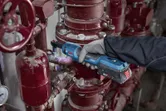 Une personne portant un équipement de sécurité utilise une clé à cliquet sans fil sur une tuyauterie industrielle.
