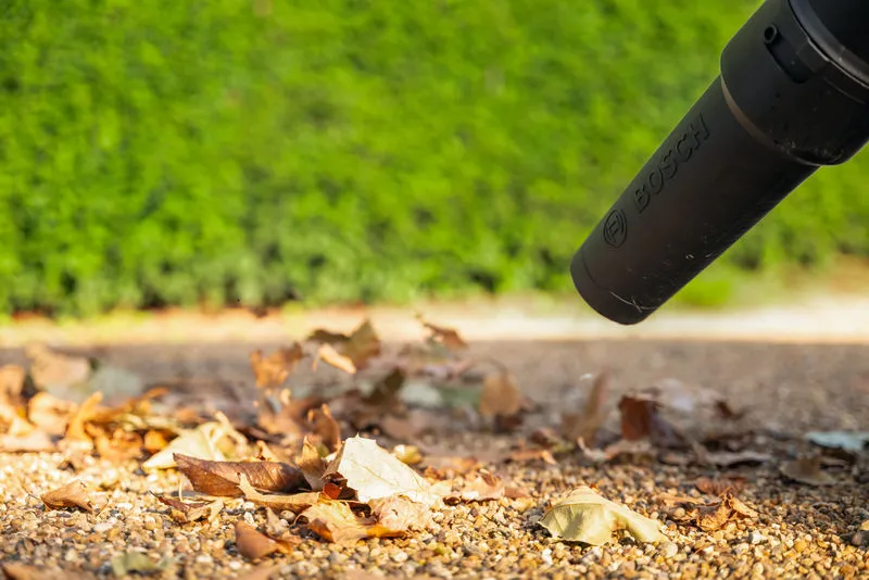 La buse de soufflage électrique déplace les feuilles sèches sur un chemin de gravier à l'extérieur.