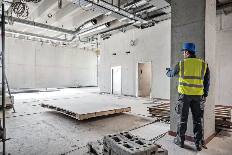 Une personne portant un équipement de sécurité utilise un télémètre laser dans un grand bâtiment en construction.