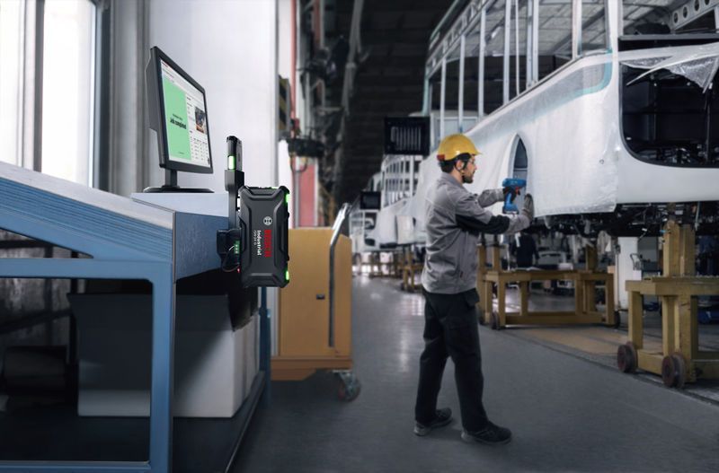 Une personne portant un équipement de sécurité utilise un outil électrique pour assembler le châssis d'un véhicule en usine.