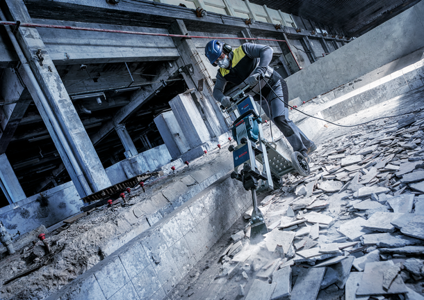 Une personne portant un équipement de sécurité démolit un sol en béton dans un environnement industriel.