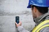 Une personne portant un équipement de sécurité utilise un humidimètre sur un mur en béton.