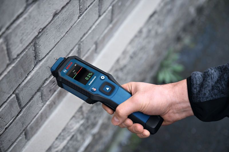 Une personne utilise un humidimètre pour vérifier l’humidité dans un mur de briques.