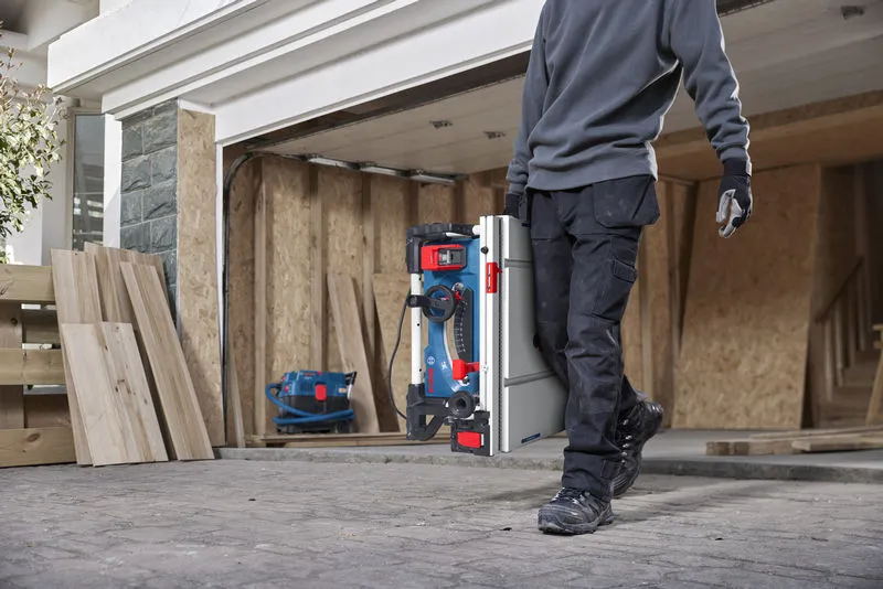Une personne portant un équipement de sécurité transporte une scie à table portative sur un chantier de construction.