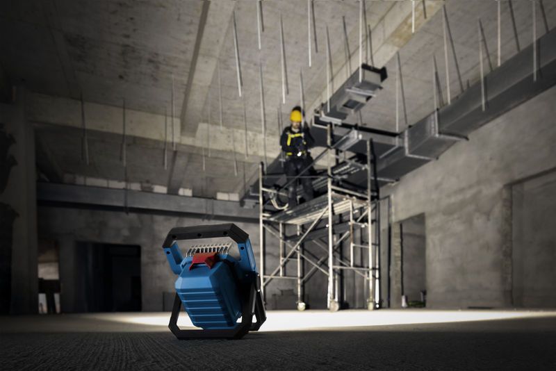 Lampe de chantier sans fil éclairant une personne portant un équipement de sécurité sur un échafaudage.