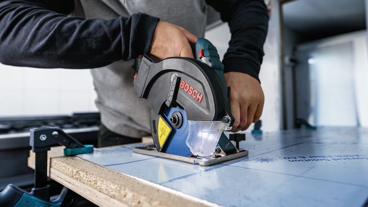 Personne utilisant une scie circulaire pour couper une planche fixée sur un établi.