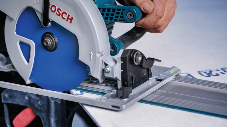 Une personne guide une scie circulaire à lame bleue le long d'une rainure droite sur une surface de travail.