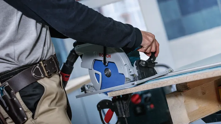 Une personne portant un équipement de sécurité utilise une scie circulaire pour couper une planche de bois.