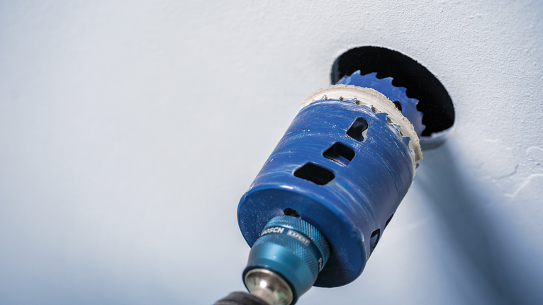 Outil électrique avec une scie cloche perçant une ouverture circulaire dans un mur.