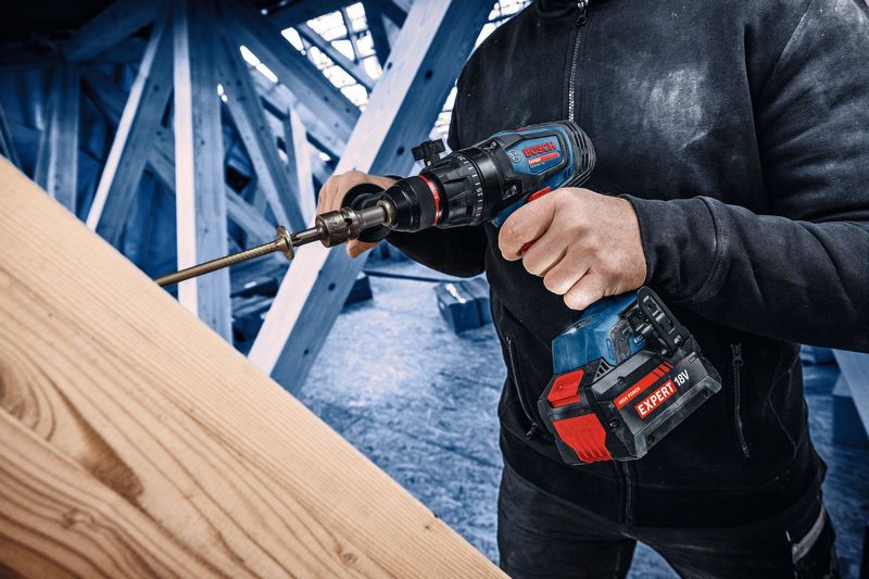 Une personne utilisant une perceuse combinée sans fil pour faire un trou dans une poutre en bois.