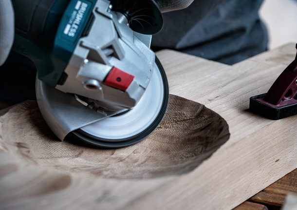 Une personne portant un équipement de sécurité utilise une meuleuse d'angle pour sculpter une surface en bois.
