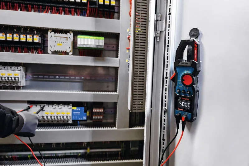 Une personne portant un équipement de sécurité teste les connexions électriques à l’aide d’une pince ampèremétrique.