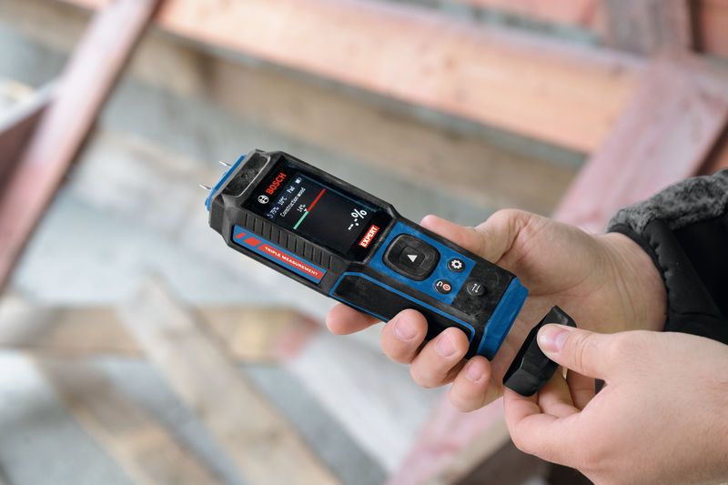 Une personne tient un humidimètre pour matériaux et se prépare à mesurer l'humidité sur un chantier de construction.