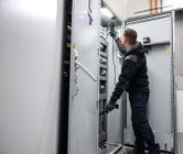 Une personne portant un équipement de sécurité teste un panneau électrique avec un testeur de tension.